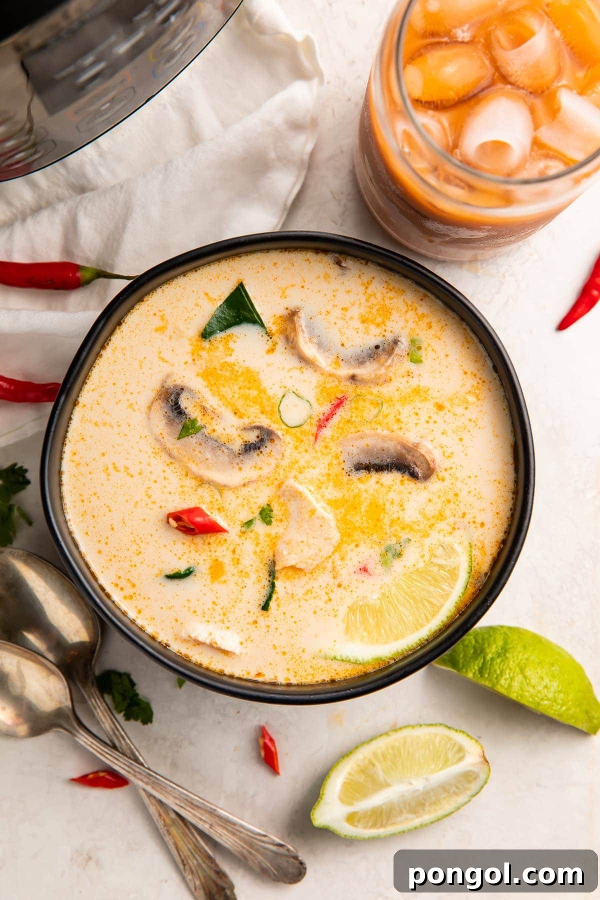 Overhead view of Instant Pot tom kha soup in a black bowl surrounded by limes and peppers