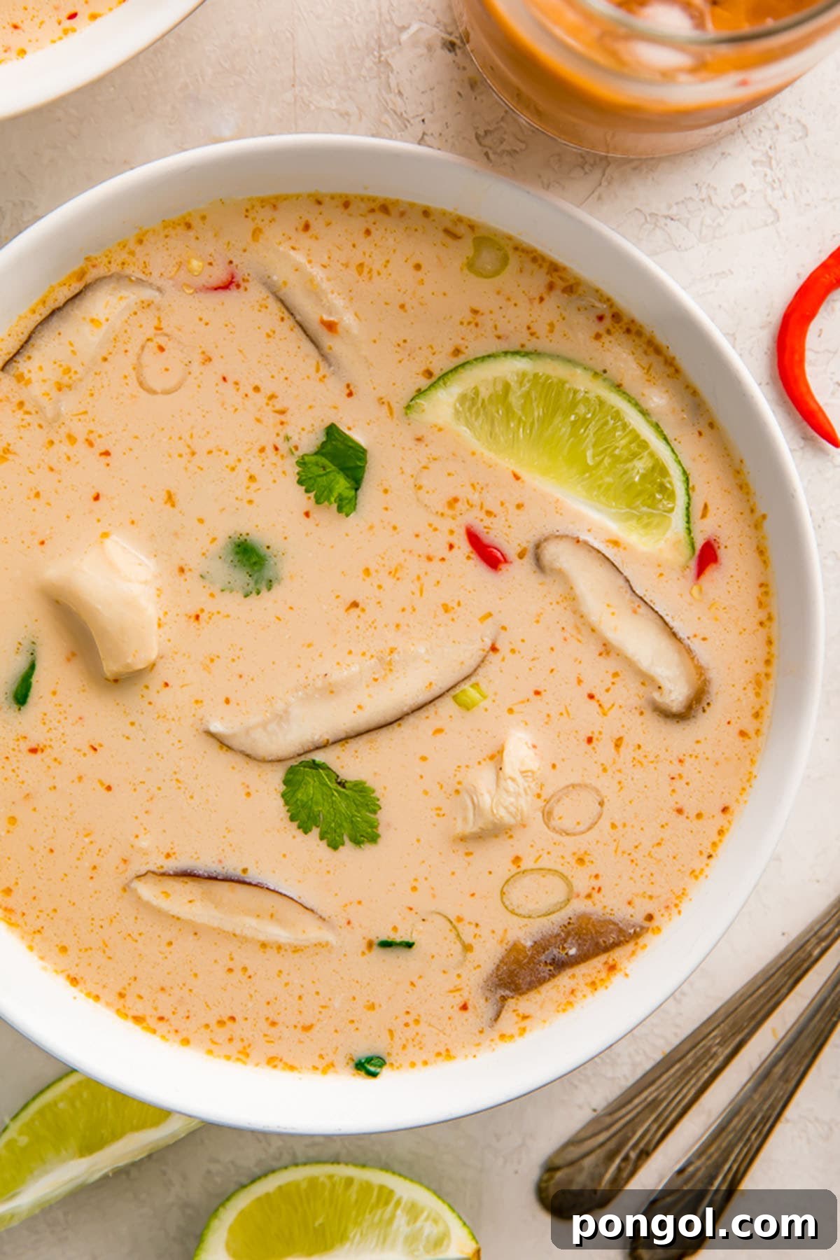 A close-up of Tom Kha Gai soup in a white bowl, garnished with fresh cilantro and a lime wedge, ready to be enjoyed.
