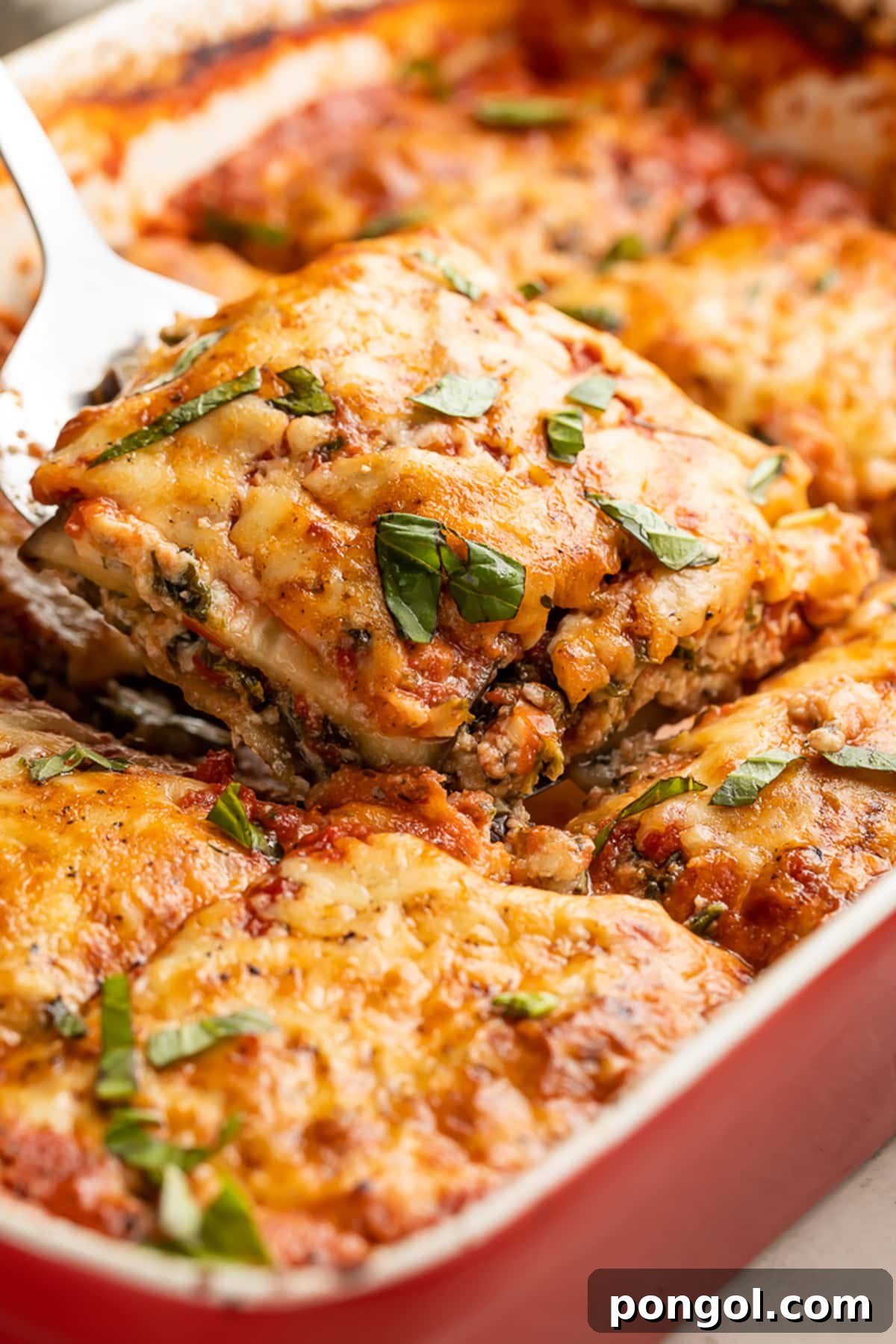 A square of eggplant lasagna being lifted out of a casserole dish of lasagna, showcasing the layers of eggplant, cheese, and sauce.