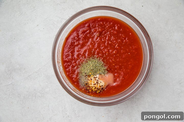 Crushed tomatoes and spices for homemade marinara in a large glass bowl.