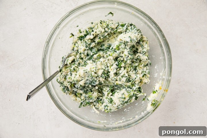 Creamy ricotta cheese and spinach filling mixture in a large glass mixing bowl.