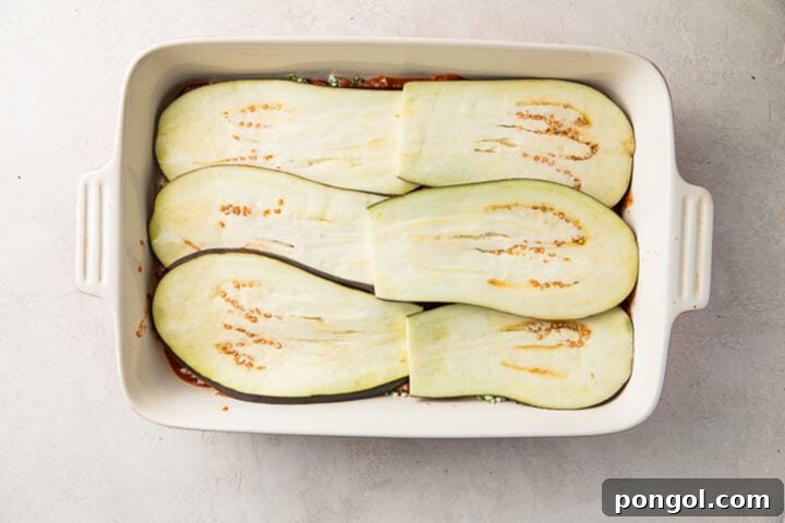 Second layer of 6 thinly-sliced eggplant slices on top of ricotta and marinara in a casserole dish.