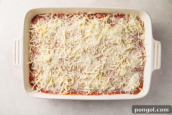 Eggplant lasagna, topped with shredded mozzarella and grated parmesan, in a rectangular white baking dish.
