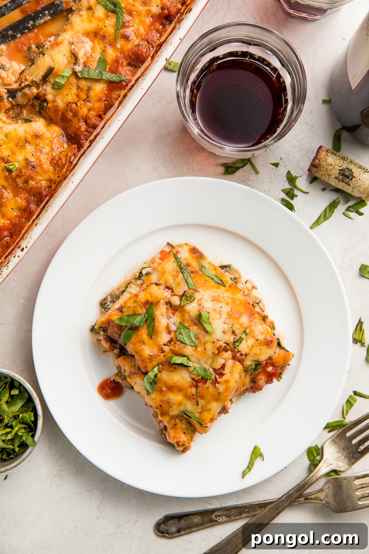A square of eggplant lasagna on a white plate next to a casserole dish of eggplant lasagna, highlighting the delicious texture and layers.