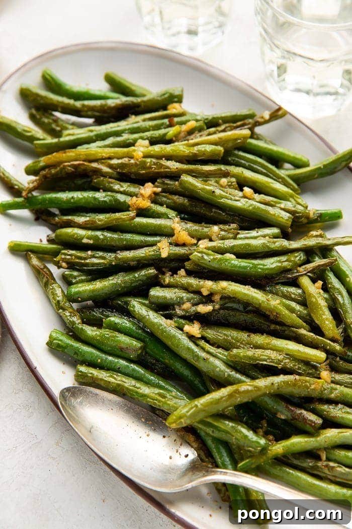 Overhead shot of a long oval plate of green beans with a silver serving spoon