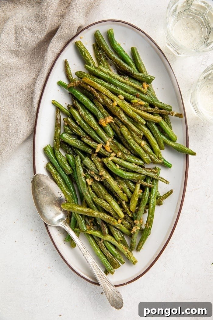 Overhead shot of an oval plate of green beans with a silver serving spoon