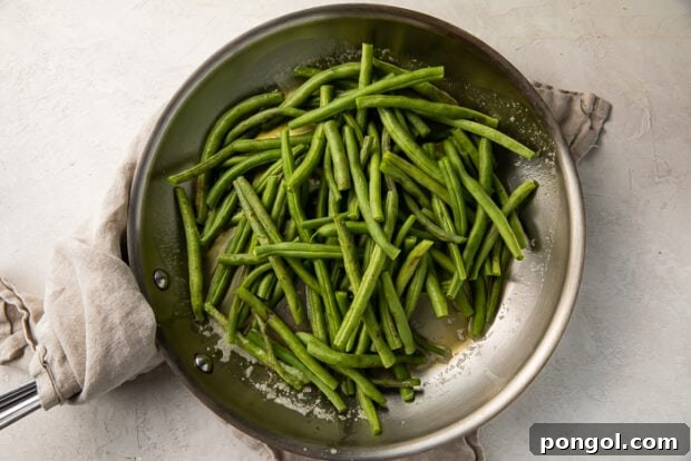 Overhead view of sauteed green beans in a large silver skillet