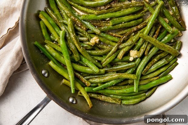 overhead shot of a skillet with cooked green beans, lemon zest, and garlic