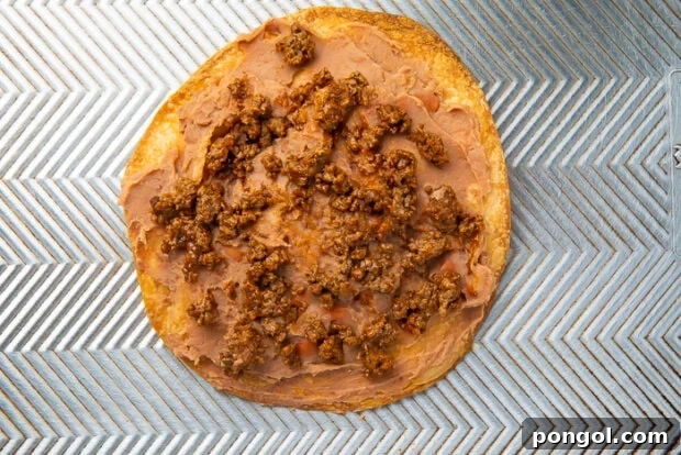 Ground beef and refried beans spread on a baking tortilla