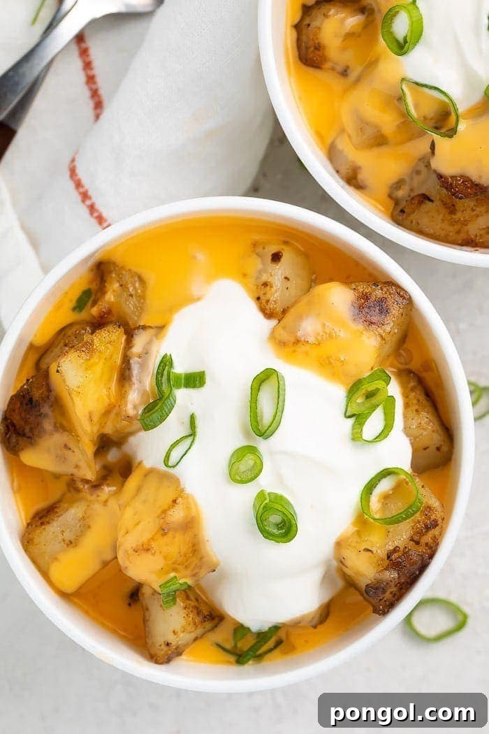 Overhead shot of potato cubes in a bowl covered with nacho cheese and sour cream with sliced green onions