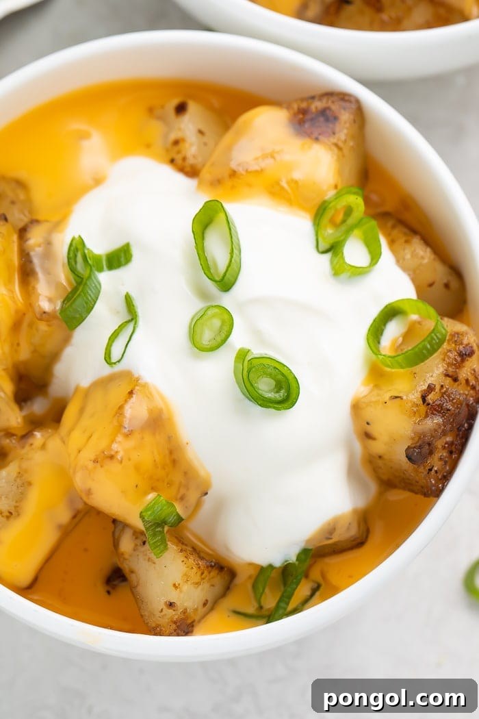 Close-up of cheesy fiesta potatoes in a bowl with a dollop of sour cream and sliced green onions