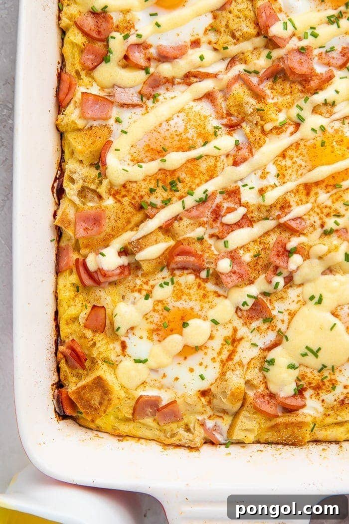 A baked eggs benedict casserole in a baking dish drizzled with a zig-zag of hollandaise sauce