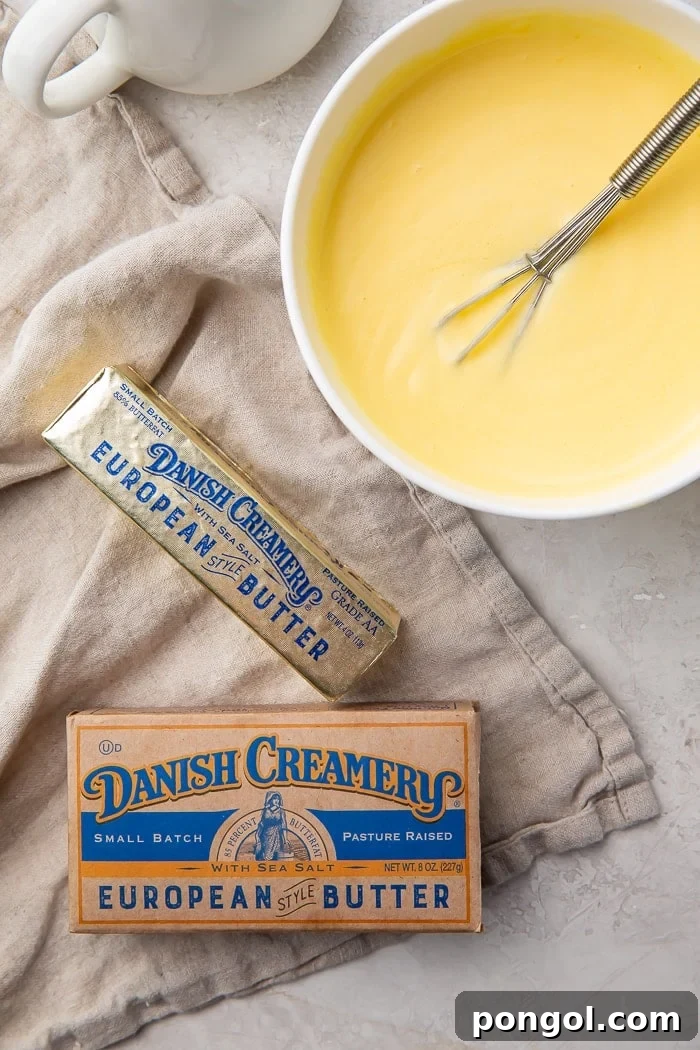 A bowl of hollandaise sauce with a whisk in it surrounded by a kraft box of butter and a stick of Danish Creamery butter