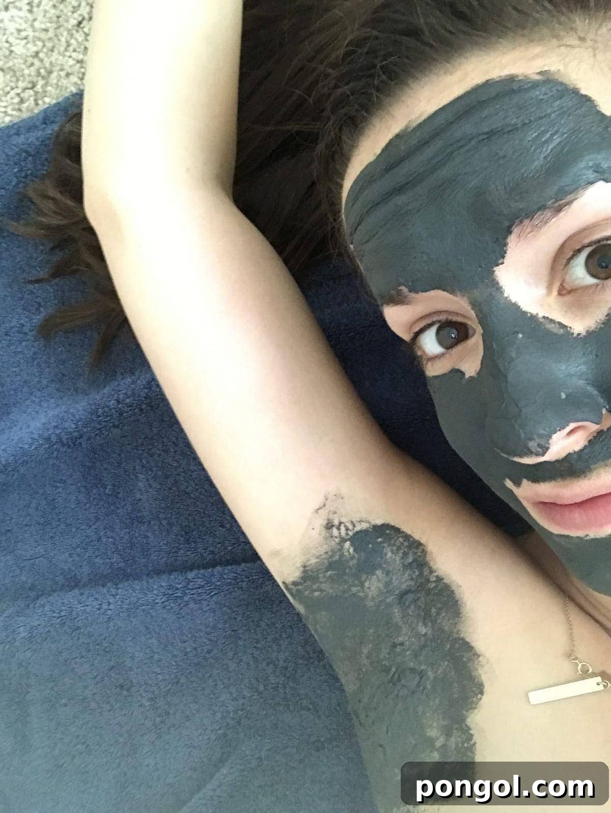 Cheryl lying on a towel with her arm above her head, with a charcoal mask applied to her face and her underarm before using natural deodorant