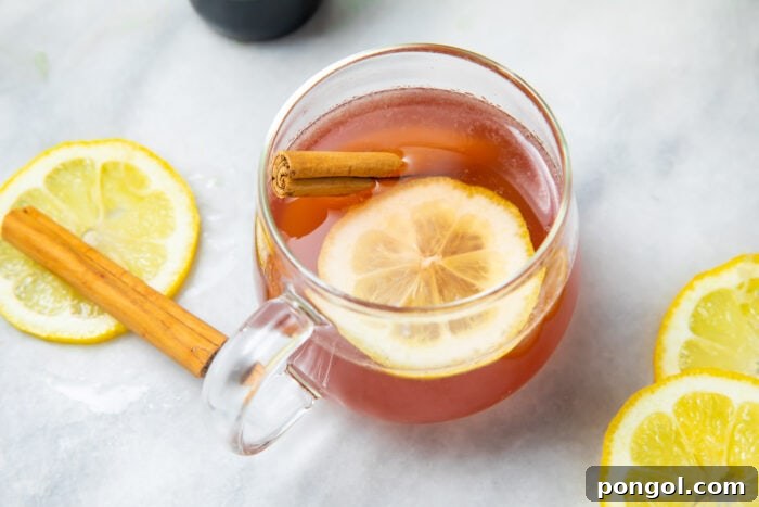 An elderberry hot toddy on a white tablecloth next to a cinnamon stick and lemon slices