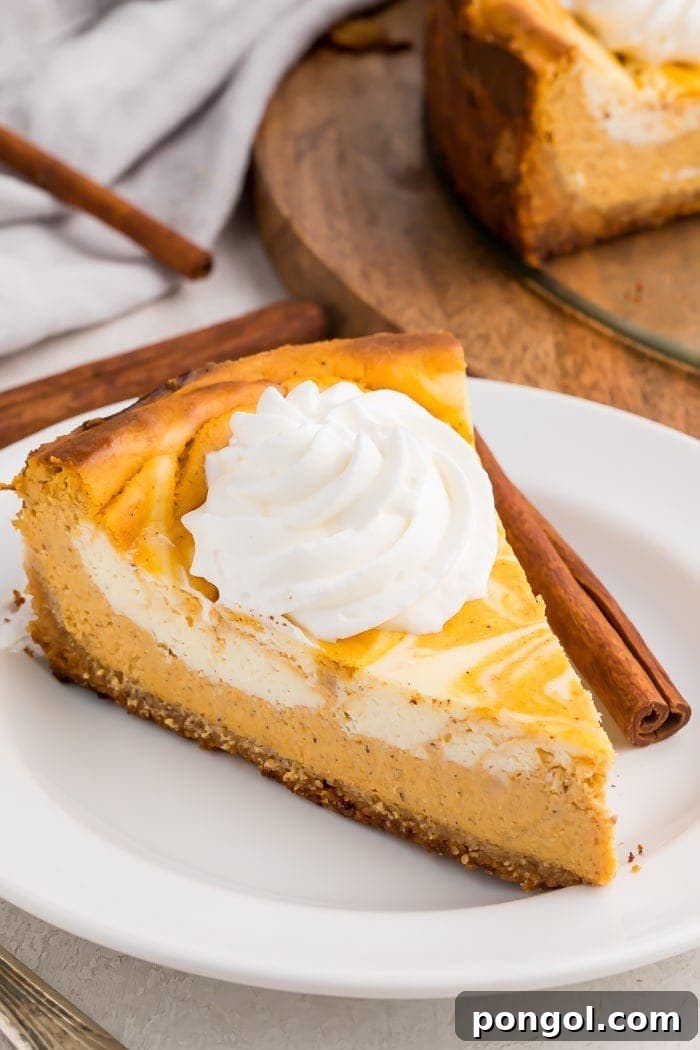 Decadent Keto Pumpkin Cheesecake 2 A slice of keto pumpkin cheesecake with a dollop of whipped cream on a white plate with a cinnamon stick