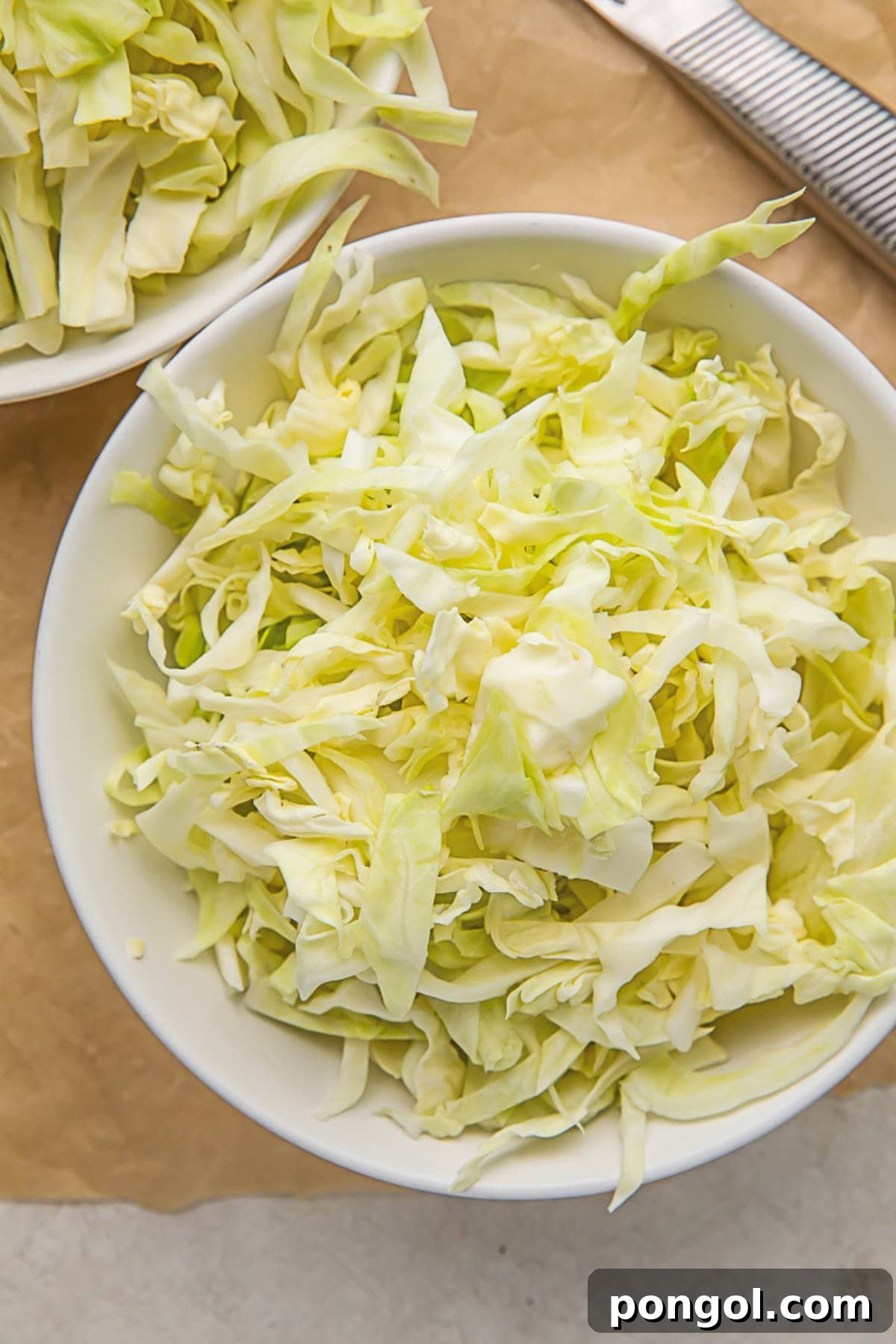 Pieces of shredded cabbage in a white bowl sitting on a wooden cutting board.