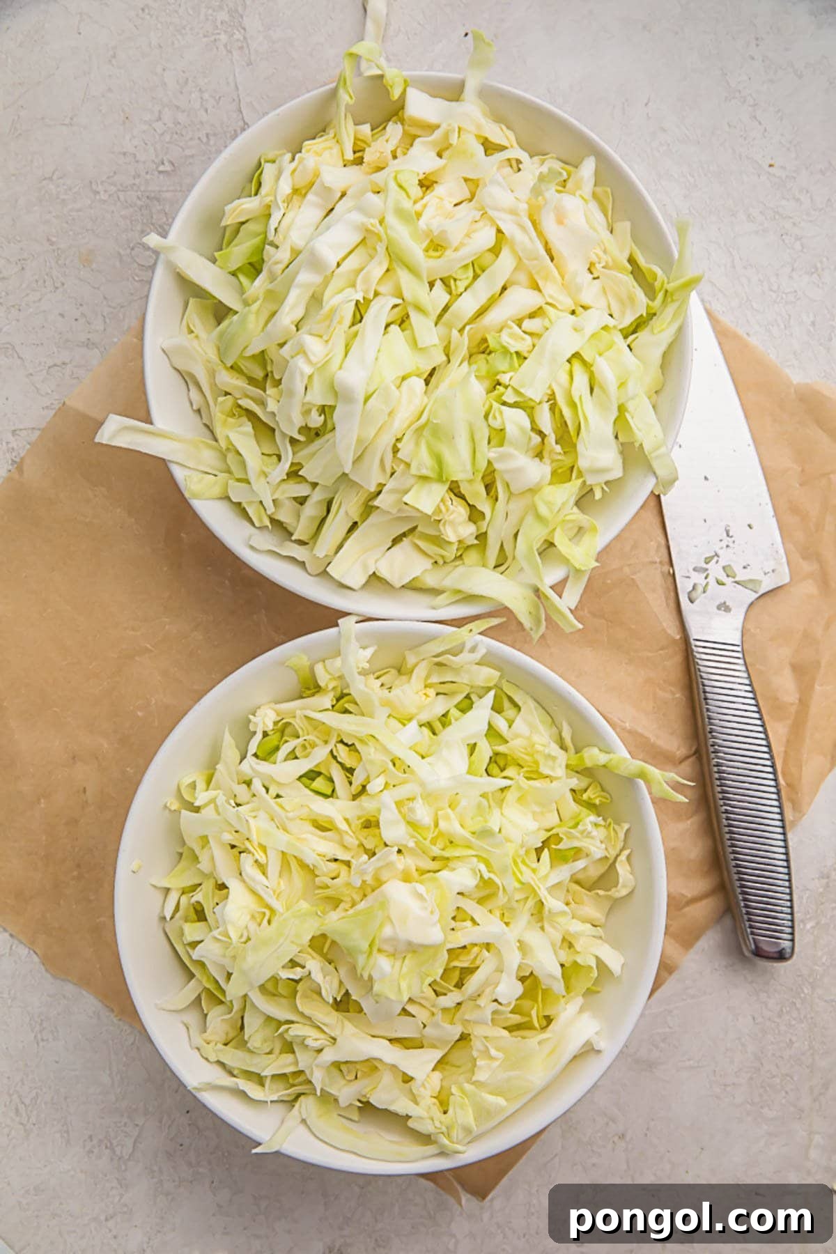 Pieces of shredded cabbage in two white bowls sitting on a wooden cutting board.