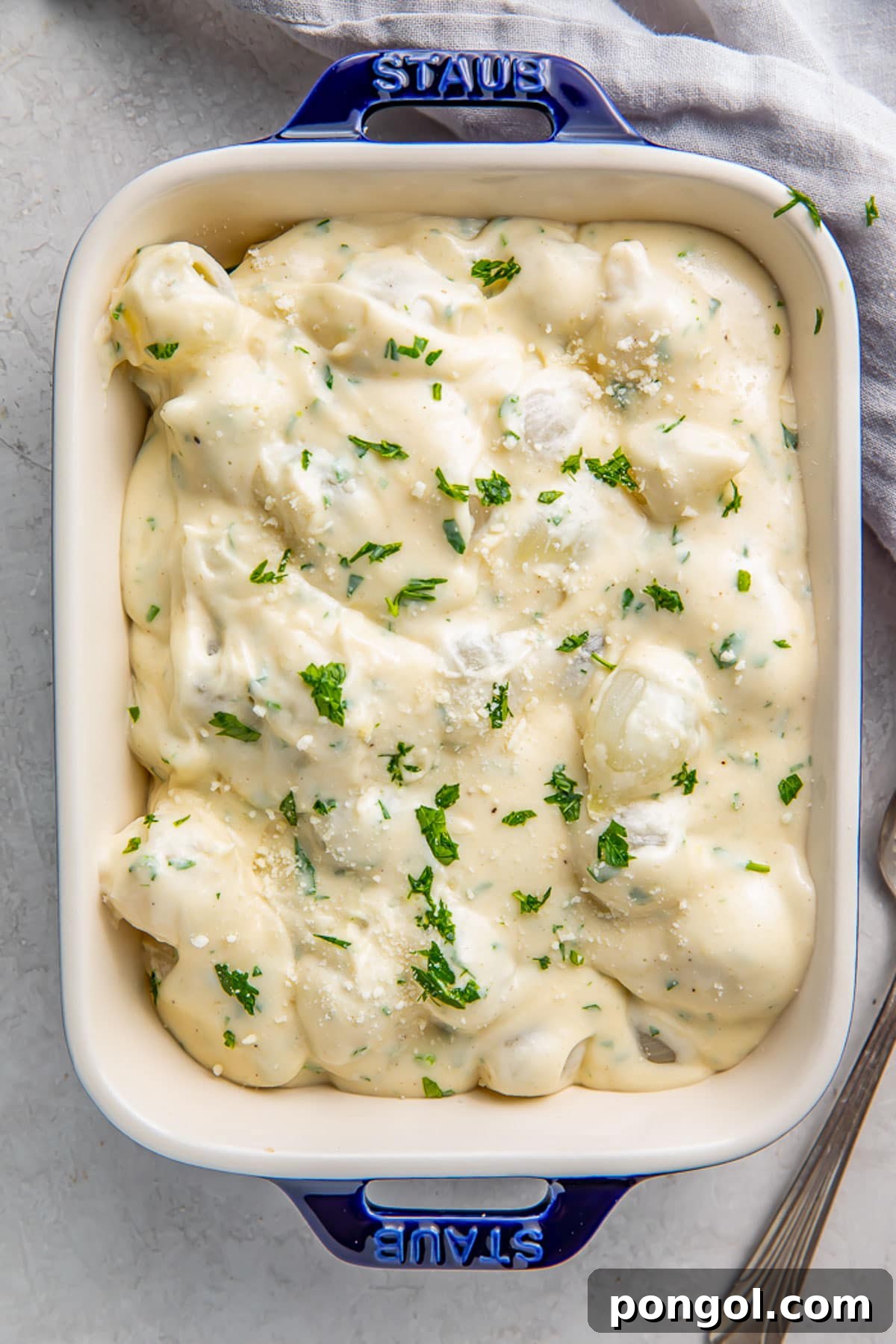 Velvety Creamed Onions 3 Overhead photo of a casserole dish holding rich creamed onions garnished with fresh herbs.