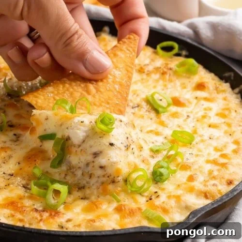 A hand dipping a chip into a cast iron skillet of crab rangoon dip