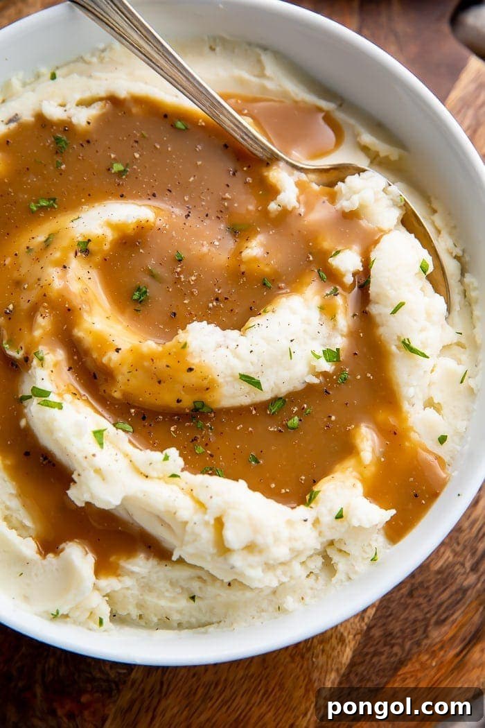 Mashed potatoes in a bowl with a spoon swirled with homemade brown gravy, looking rich and creamy