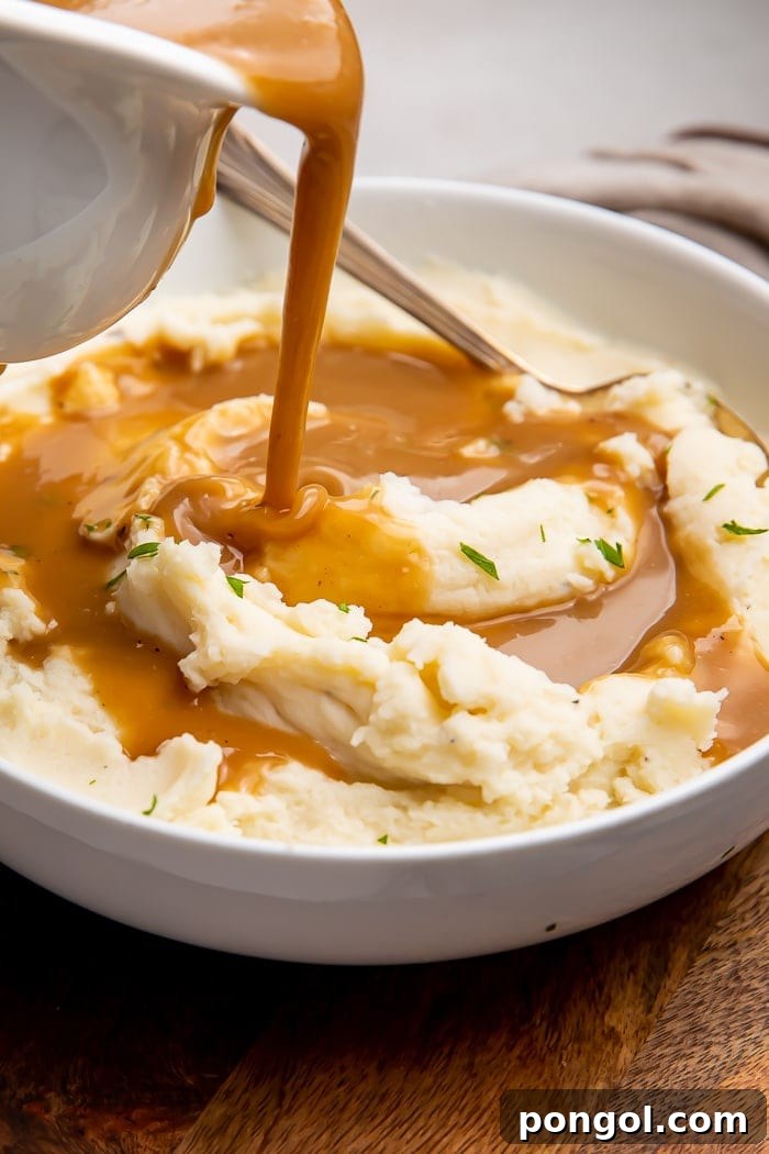 Rich, homemade brown gravy being poured generously over a mound of creamy mashed potatoes, ready to be enjoyed
