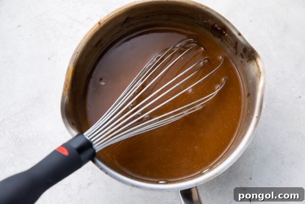 Ingredients for brown gravy being whisked together in a saucepan over medium heat, including beef stock, cornstarch, and onion powder