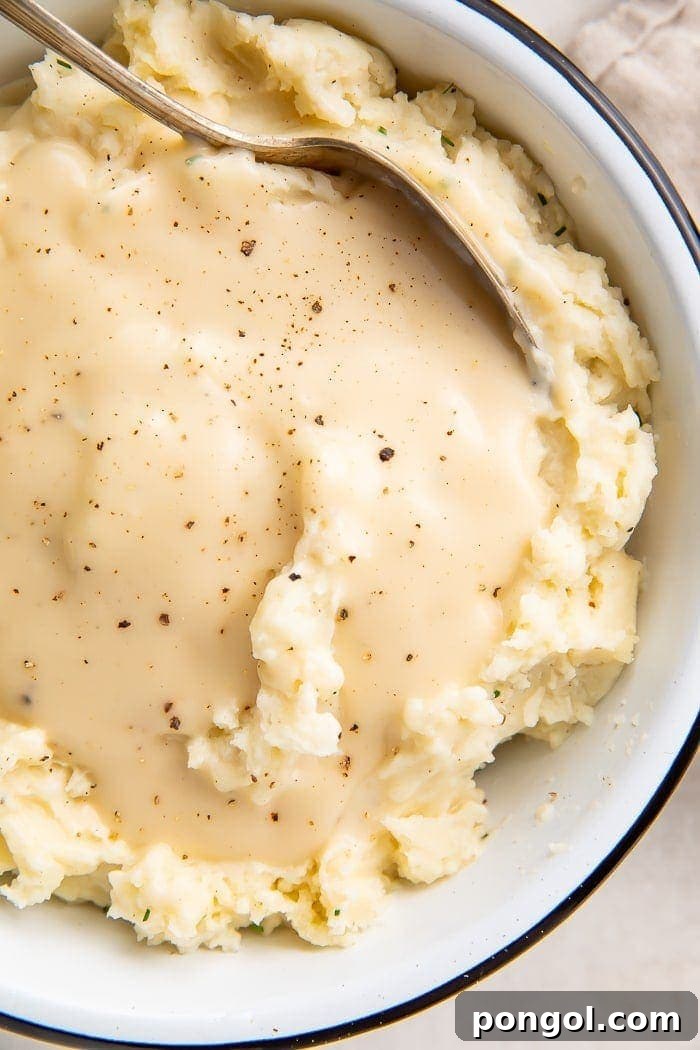Overhead shot of chicken gravy over mashed potatoes in a white bowl with a spoon