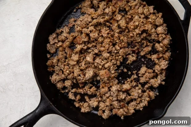 Heirloom Sausage Stuffing 7 Sausage browning in a skillet, being crumbled with a wooden spoon.