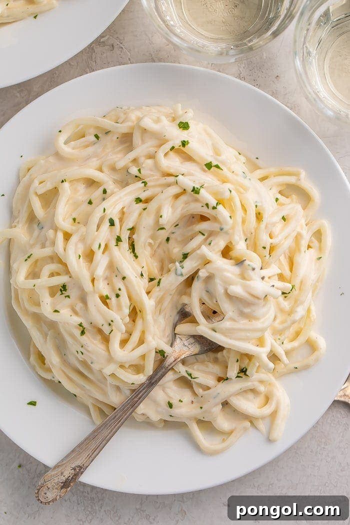 Keto Alfredo Sauce on palmini noodles, served on a white plate with a fork, emphasizing rich and creamy texture.