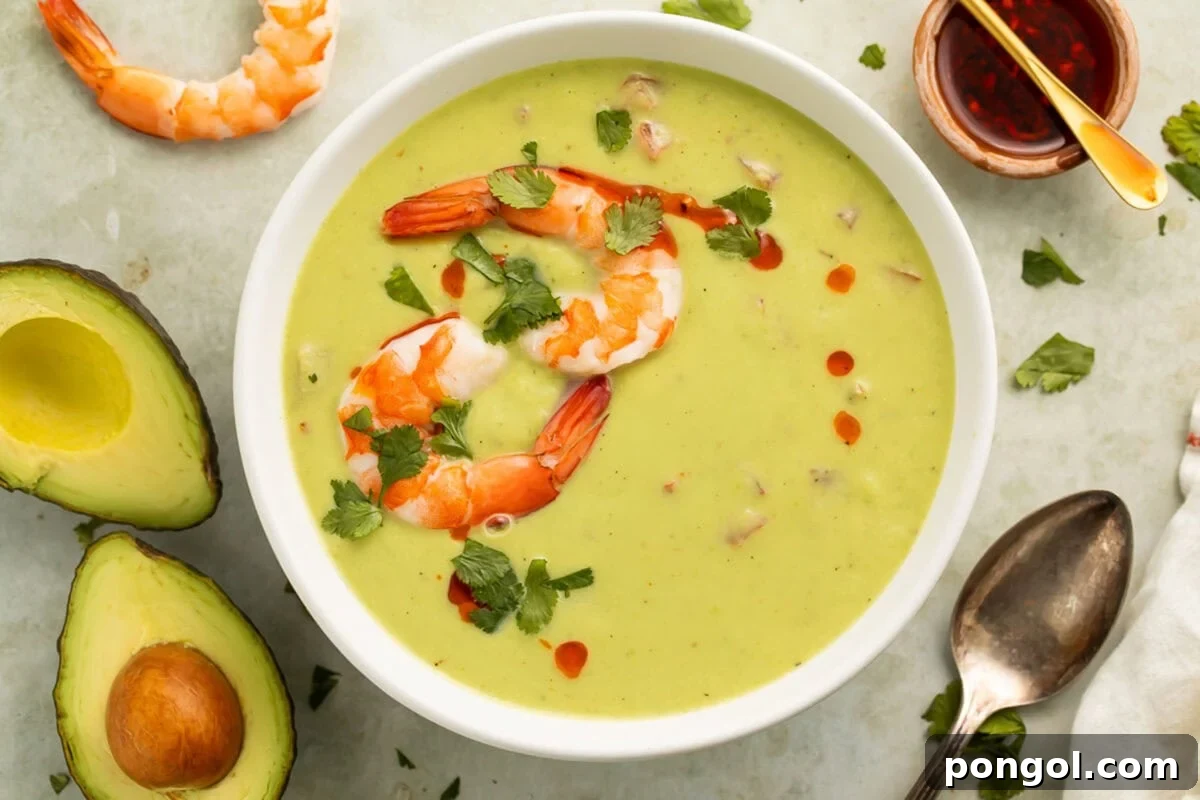 Velvety Chilled Avocado 3 A beautifully presented bowl of emerald green avocado soup, topped with bright red chili oil and succulent pink shrimp, inviting a refreshing culinary experience.