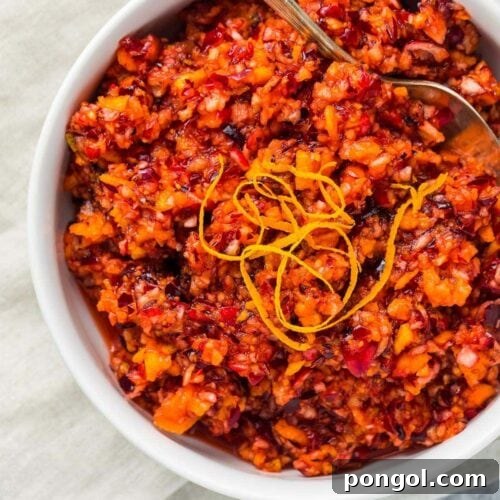 Zesty Cranberry Orange Relish 5 Bright red cranberry relish with orange peel garnish in a white bowl on a napkin and marble countertop