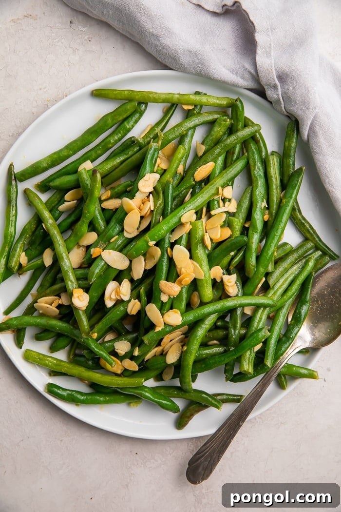 Green beans with almonds on a white platter, elegantly presented with a silver fork and white napkin.