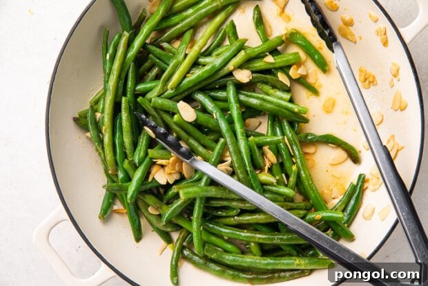 Cooked green beans being sautéed with toasted almonds, lemon juice, and zest.