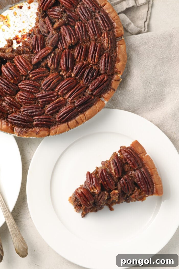 Slice of pecan pie on a white plate next to a whole pecan pie