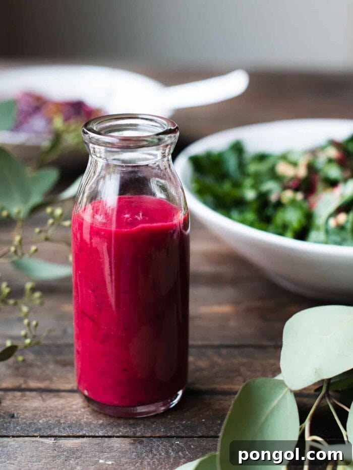 Dark red cranberry vinaigrette dressing with a bowl of salad and a wood table