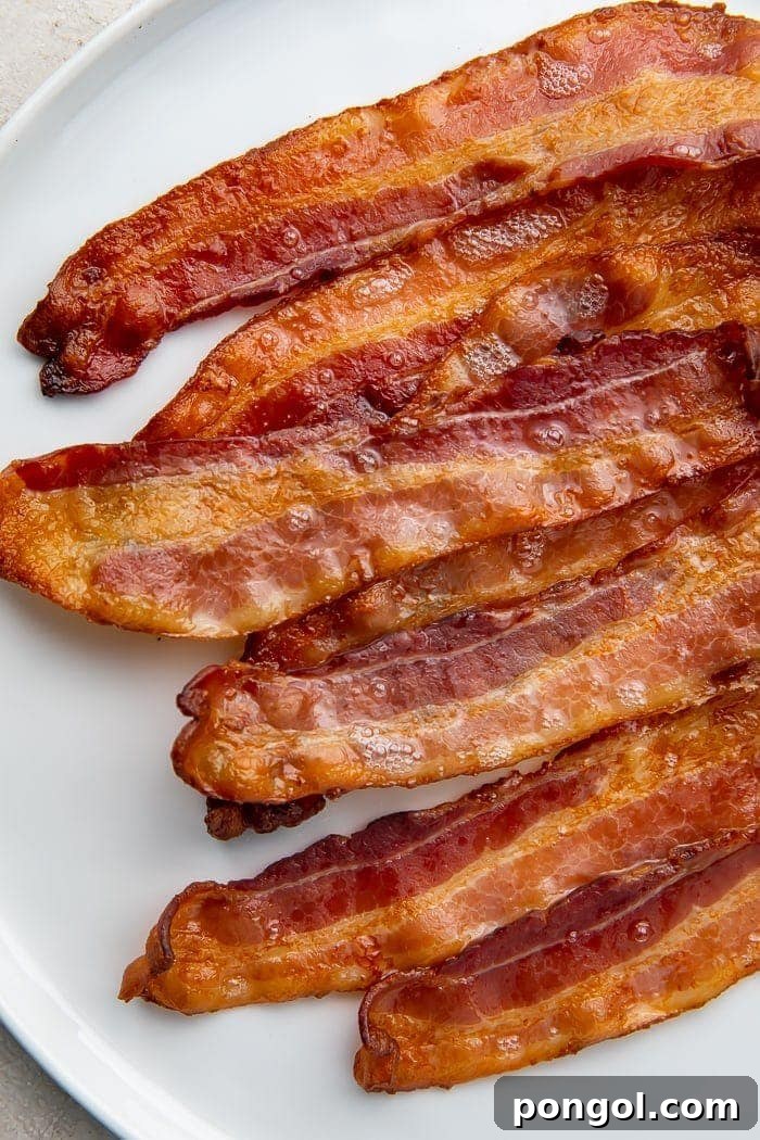 The Secret to Perfectly Crispy Oven Bacon 2 Perfectly oven-cooked bacon strips neatly arranged on a clean white plate, showcasing their golden-brown crispiness