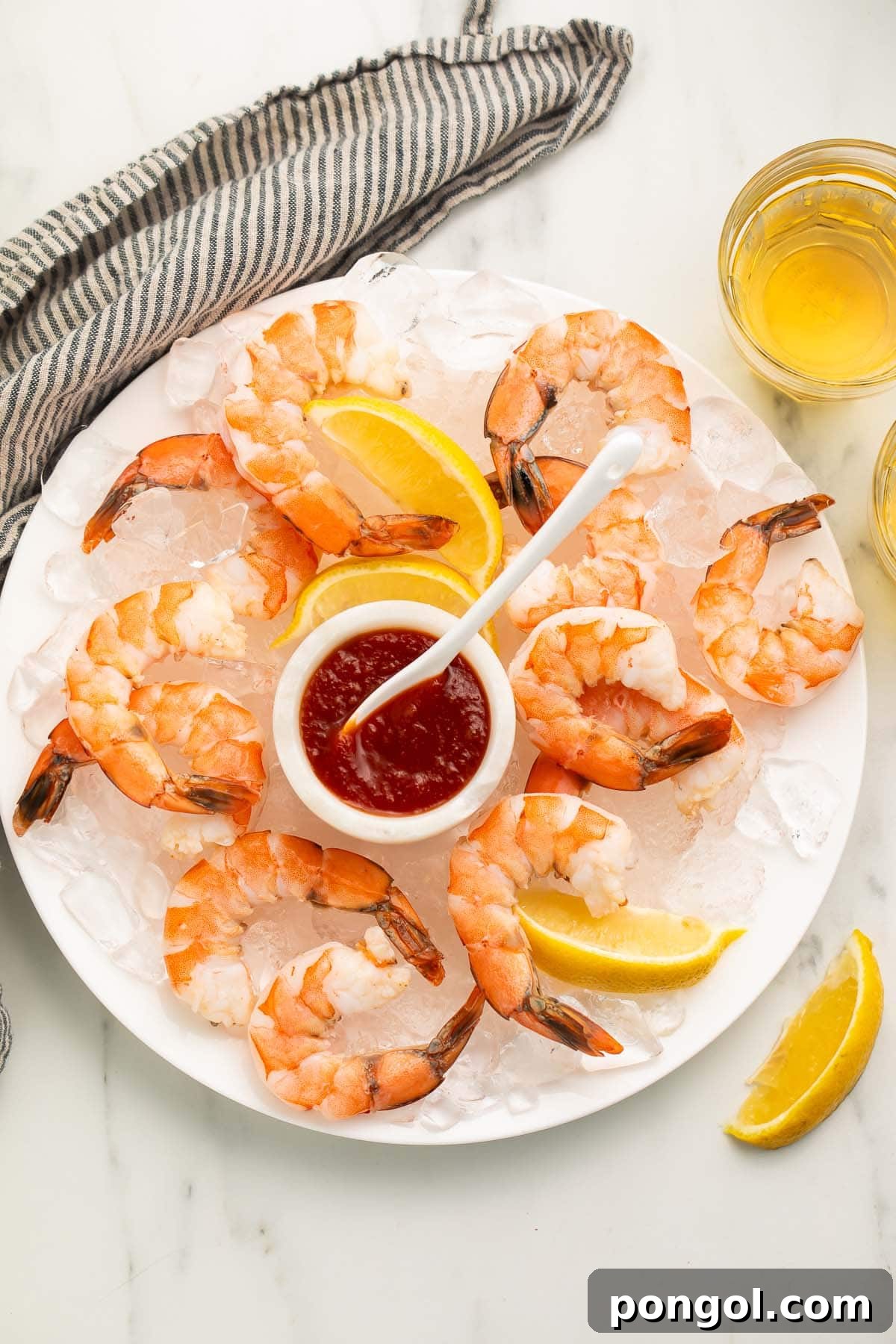 Poached shrimp arranged on a platter of ice next to a small dipping bowl of shrimp cocktail sauce.