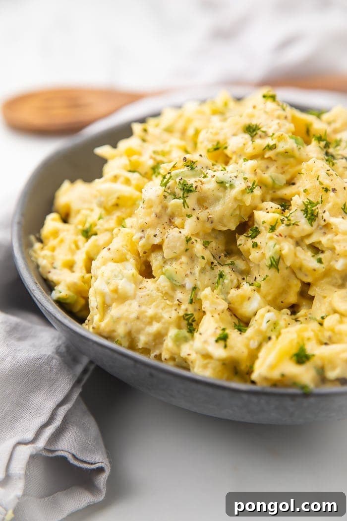 Dark serving bowl with yellow potato salad and green garnish