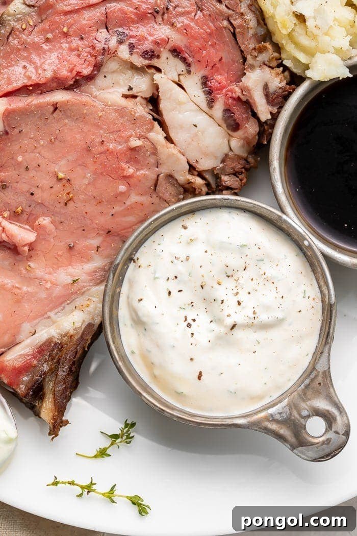 A side of creamy horseradish sauce next to a perfectly cooked prime rib on a white plate, ready to be served.