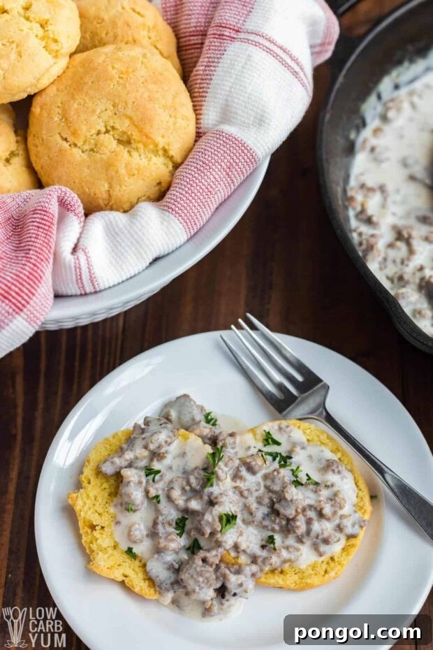 Fluffy Keto Biscuits with creamy sausage gravy on a white plate, with a basket of biscuits in the background.
