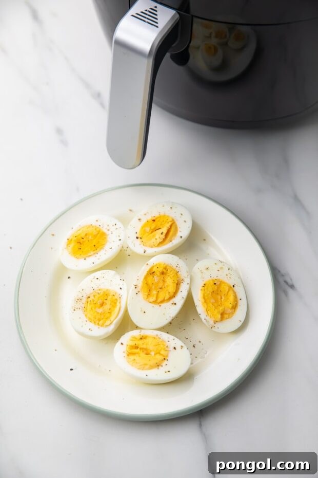 Perfectly cooked Hard Boiled Eggs on a white plate next to an air fryer.