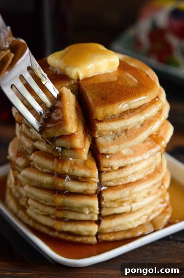 A tall stack of fluffy Keto Pancakes drizzled with sugar-free maple syrup and topped with butter.