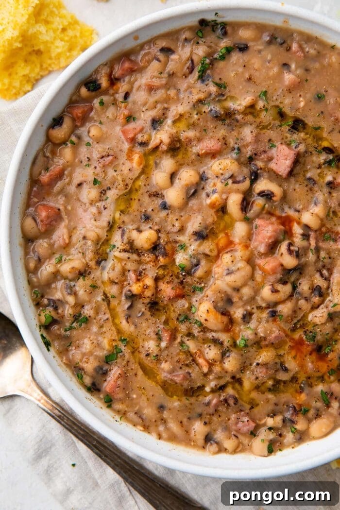 White bowl holding instant pot black eyed peas with ham, bacon, and onion, garnished with fresh herbs and a dash of hot sauce.