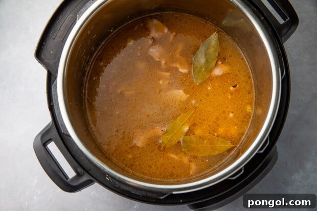 Instant Pot filled with black-eyed peas, bacon, ham, chicken stock, and bay leaves, ready for pressure cooking.