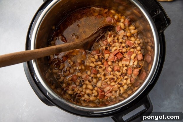 Mashing cooked Instant Pot black-eyed peas with a wooden spoon to achieve a creamy texture.