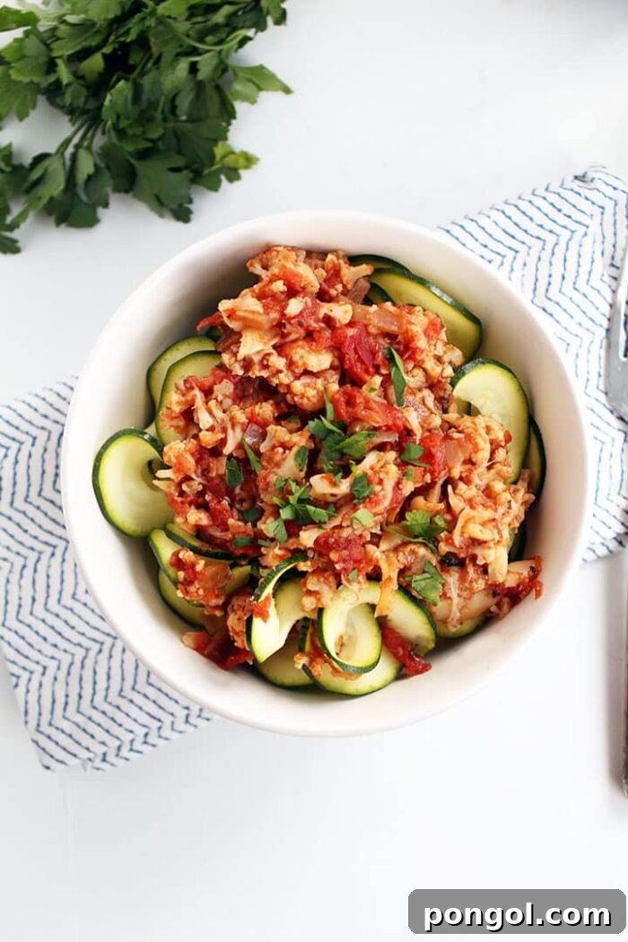A white bowl of vegetarian slow cooker crockpot cauliflower bolognese on top of zucchini noodles