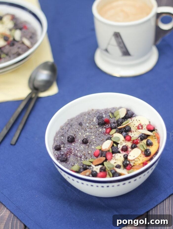 A white bowl of blueberry vegetarian slow cooker quinoa with fruits and slivers of almonds on a blue tablecloth