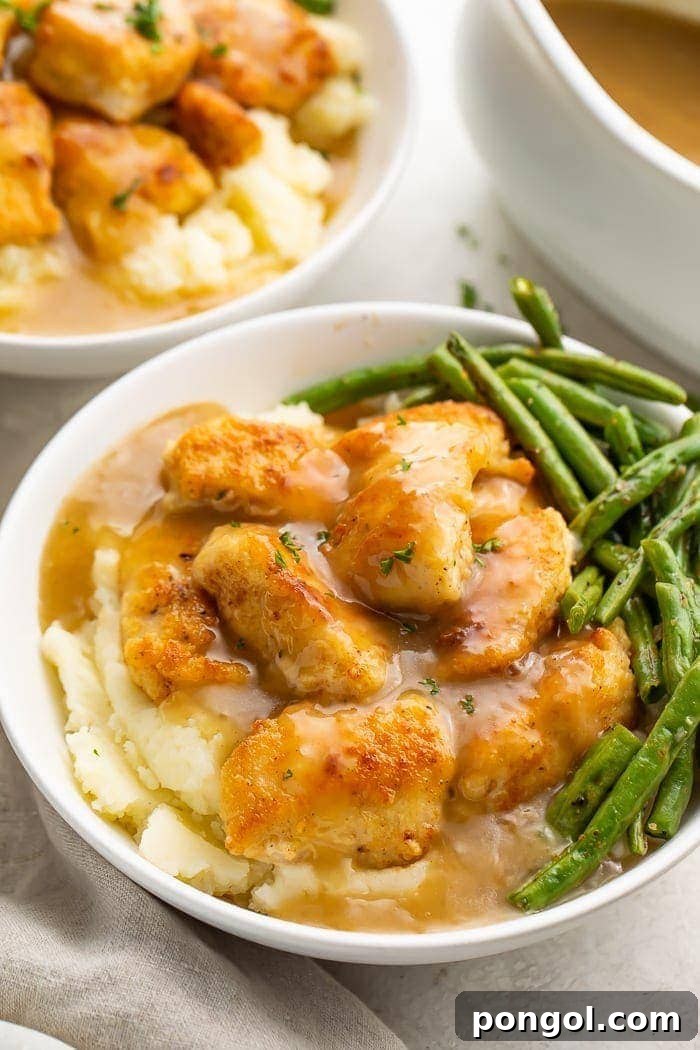 A delectable Whole30 fried chicken and mashed potato bowl, artfully arranged with gravy and green beans in a white ceramic bowl, ready to be enjoyed.
