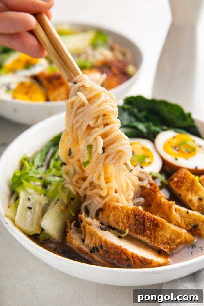 A hand holding chopsticks lifting shirataki noodles out of a white bowl of keto ramen